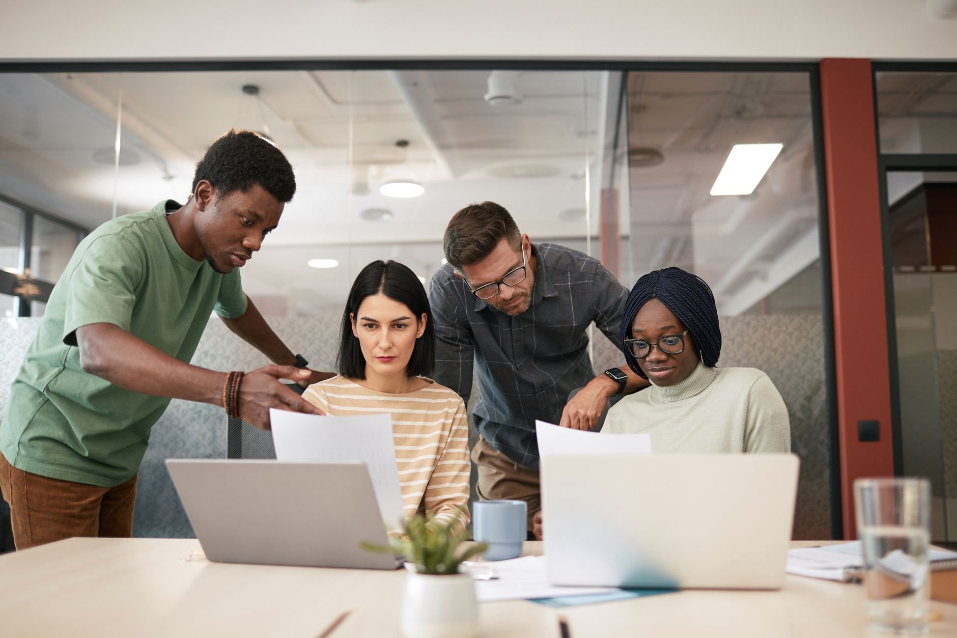 A diverse team collaborates in a modern office, reviewing candidates on laptops